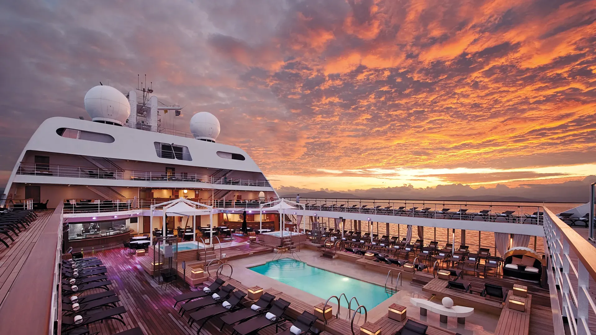 A large cruise ship with a swimming pool on the deck at sunset.