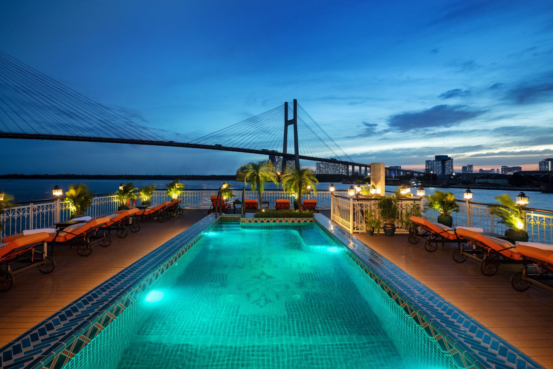 A large swimming pool is lit up at night with a bridge in the background.