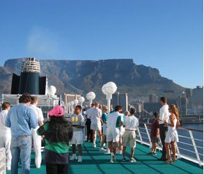 A group of people are standing on the deck of a boat with a mountain in the background.