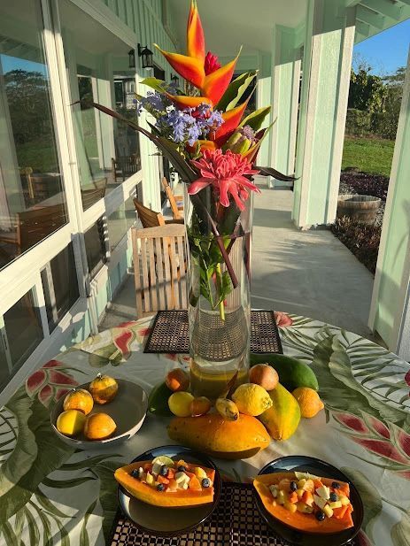 A table with tropical fruit, a flower arrangement, and a porch setting.