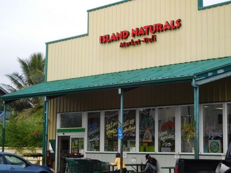 Island Naturals Market-Deli storefront with green roof, red sign, and people seated outside.