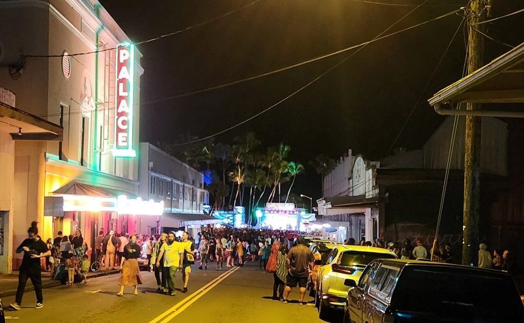 Night scene of crowded street with cars and people. Palace theater with neon sign in background.