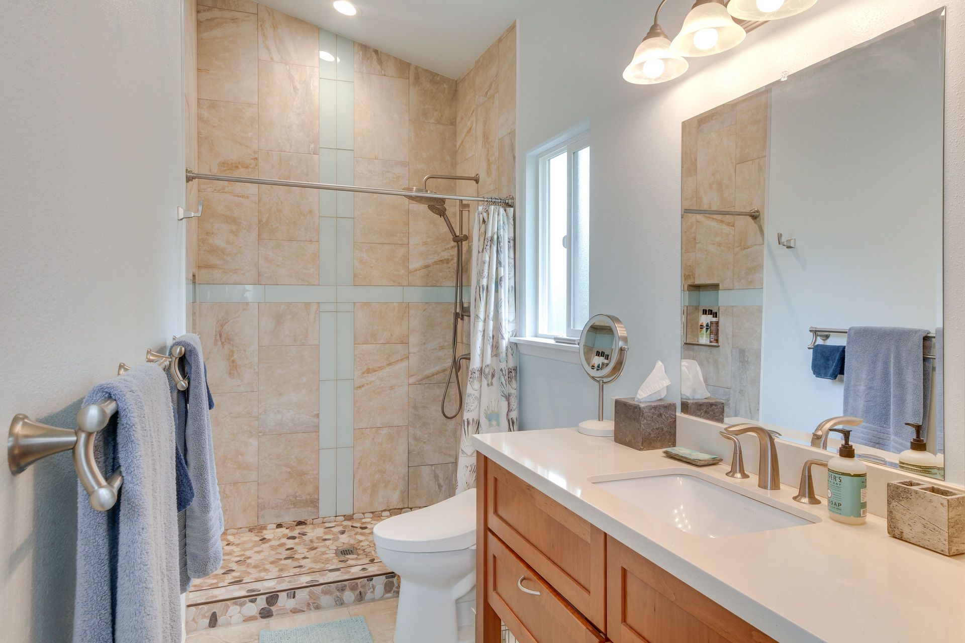 Bathroom with a walk-in shower, toilet, vanity, and large mirror. Neutral tones, towel rack with blue towels.