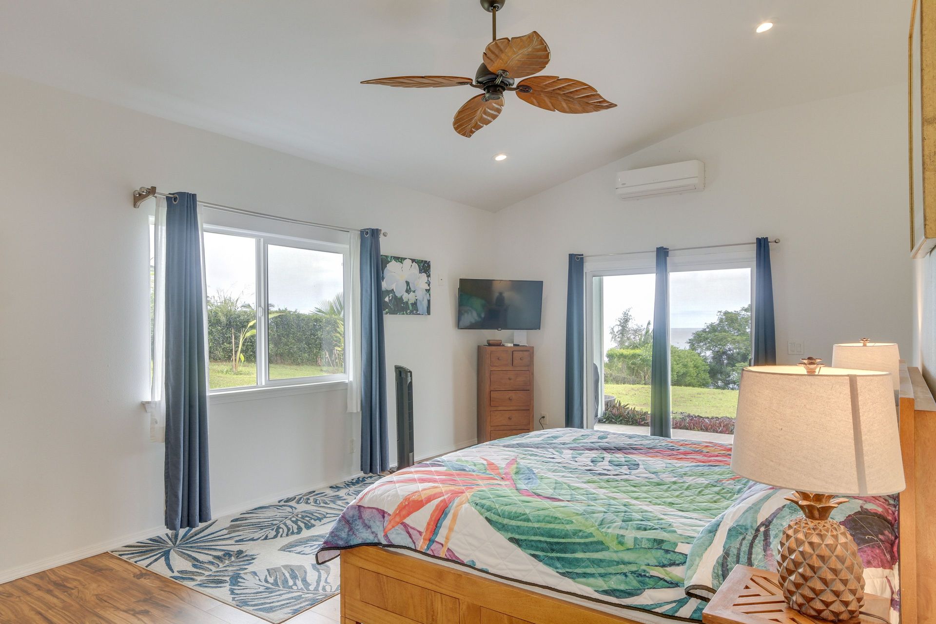 Bedroom with a bed, windows, ceiling fan, and a TV mounted on a wall.