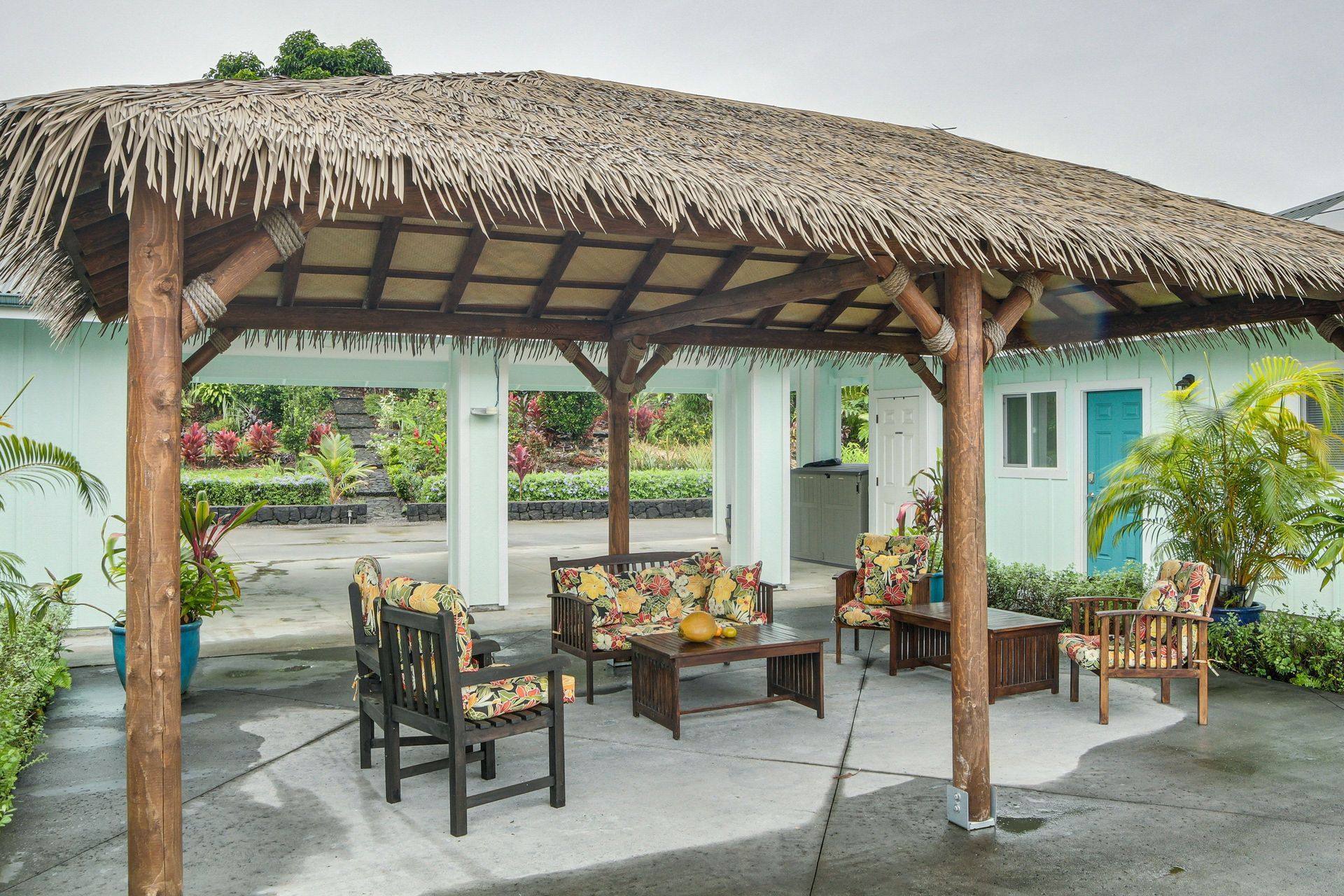 Patio with tiki-style roof, furniture, and a light blue building in the background.