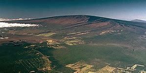 Aerial view of a large mountain with dark brown slopes and a green landscape below.