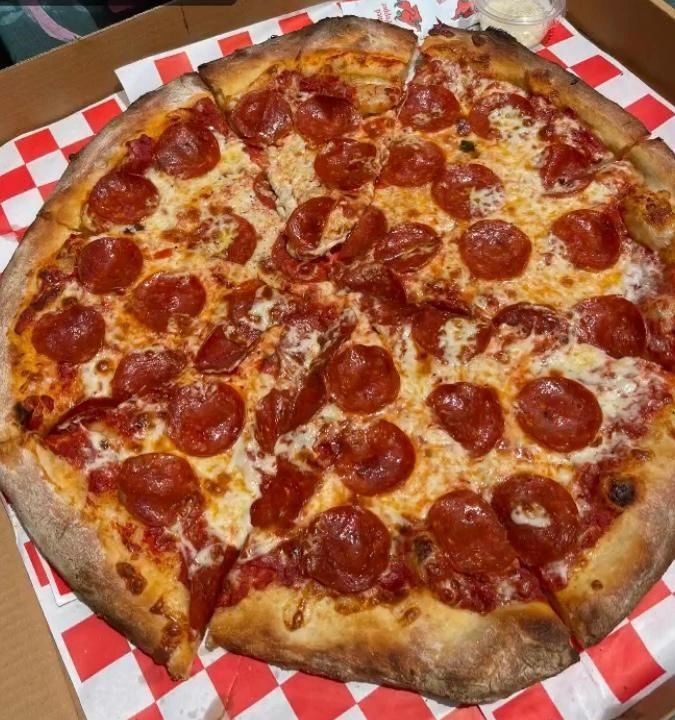 Pepperoni pizza in a box, sliced, with red checkered paper.