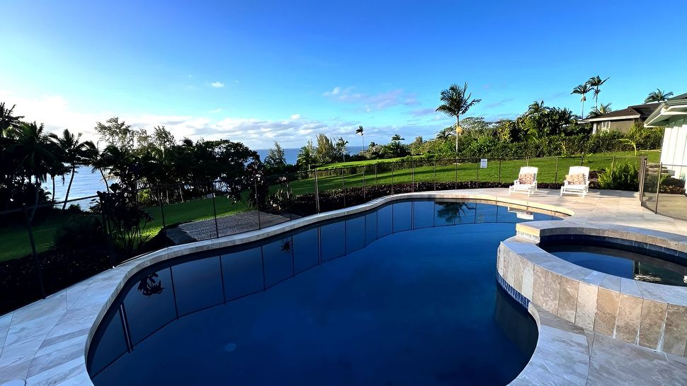 Koili Point Swimming pool overlooking ocean, palm trees, green grass, blue sky.