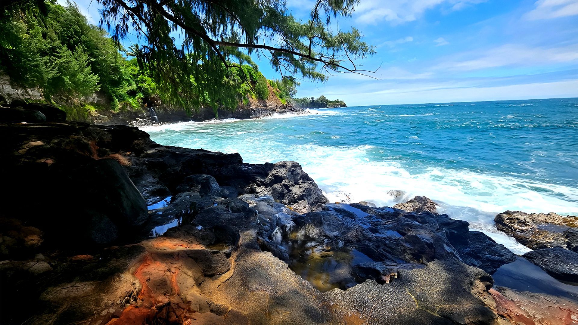 A rocky shoreline with waves crashing dramatically against the rocks under a clear blue sky.