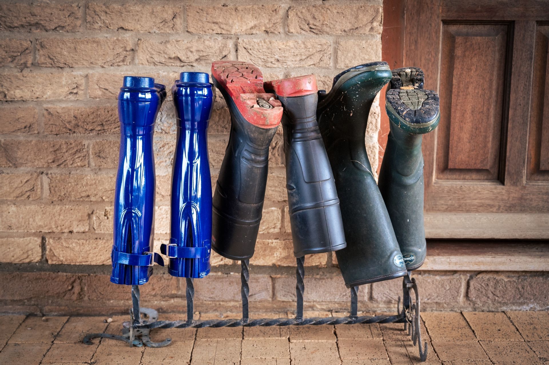 A row of boots are lined up on a rack against a brick wall.