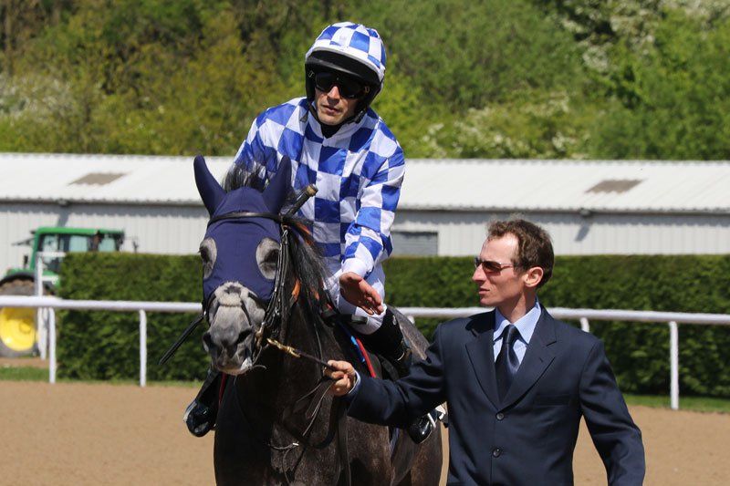 A man in a suit stands next to a jockey on a horse