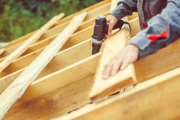 Carpenter using a drill on wooden rafters, outdoors.