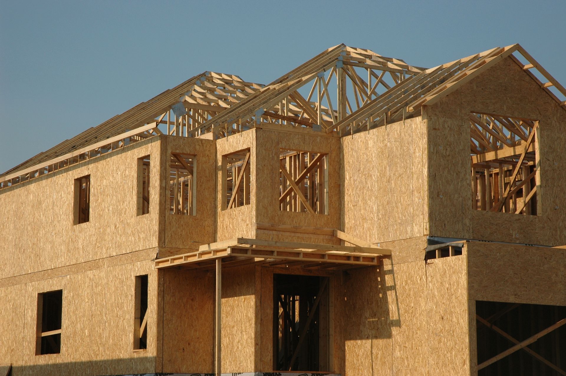 Two-story house under construction, with wooden frame and panels visible; blue sky in background.