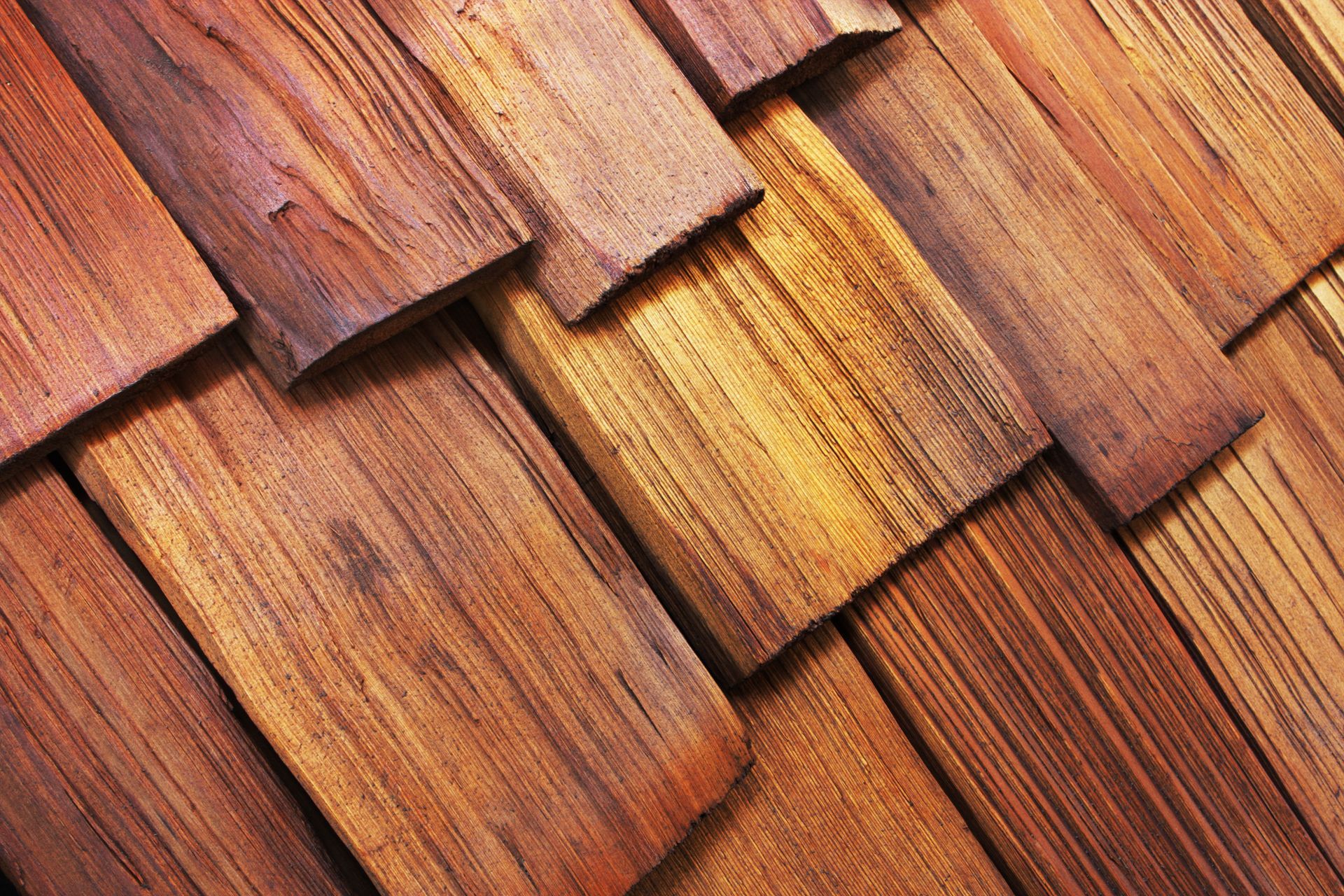 Close-up view of overlapping, textured, brown wooden shingles with varying shades and grain patterns.