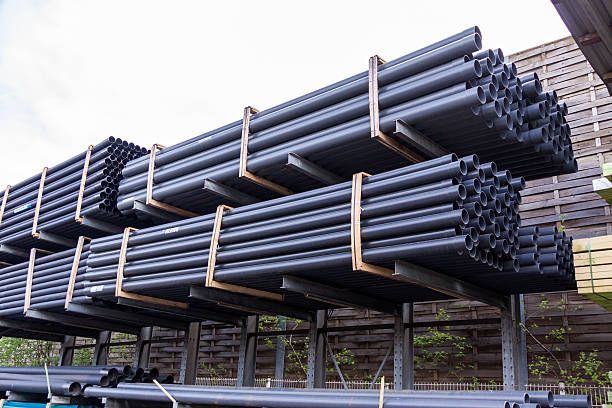 Stacks of black plastic pipes on metal shelves outdoors.