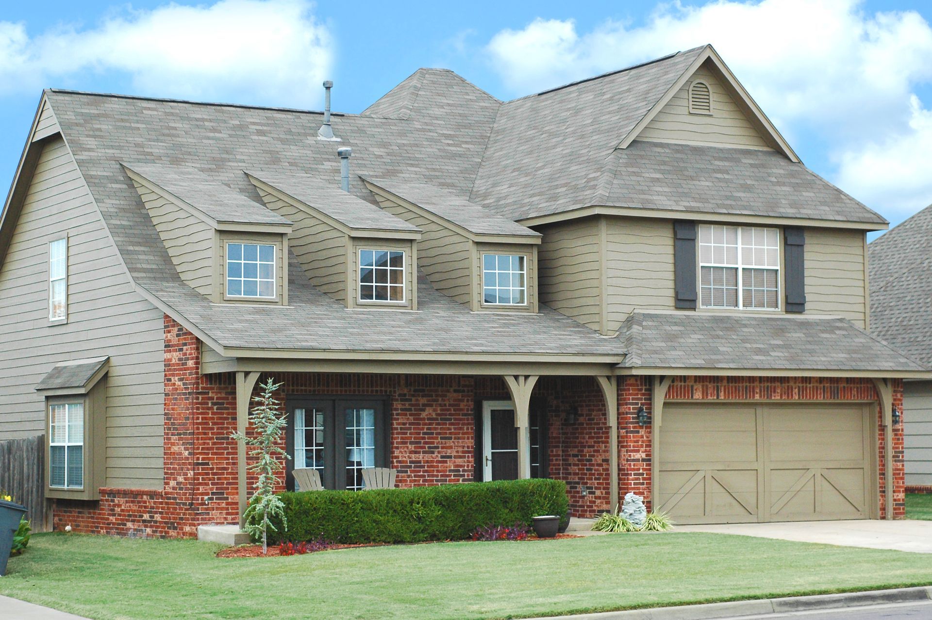 Two-story house with brick and siding exterior, front porch, and attached garage under a blue sky.