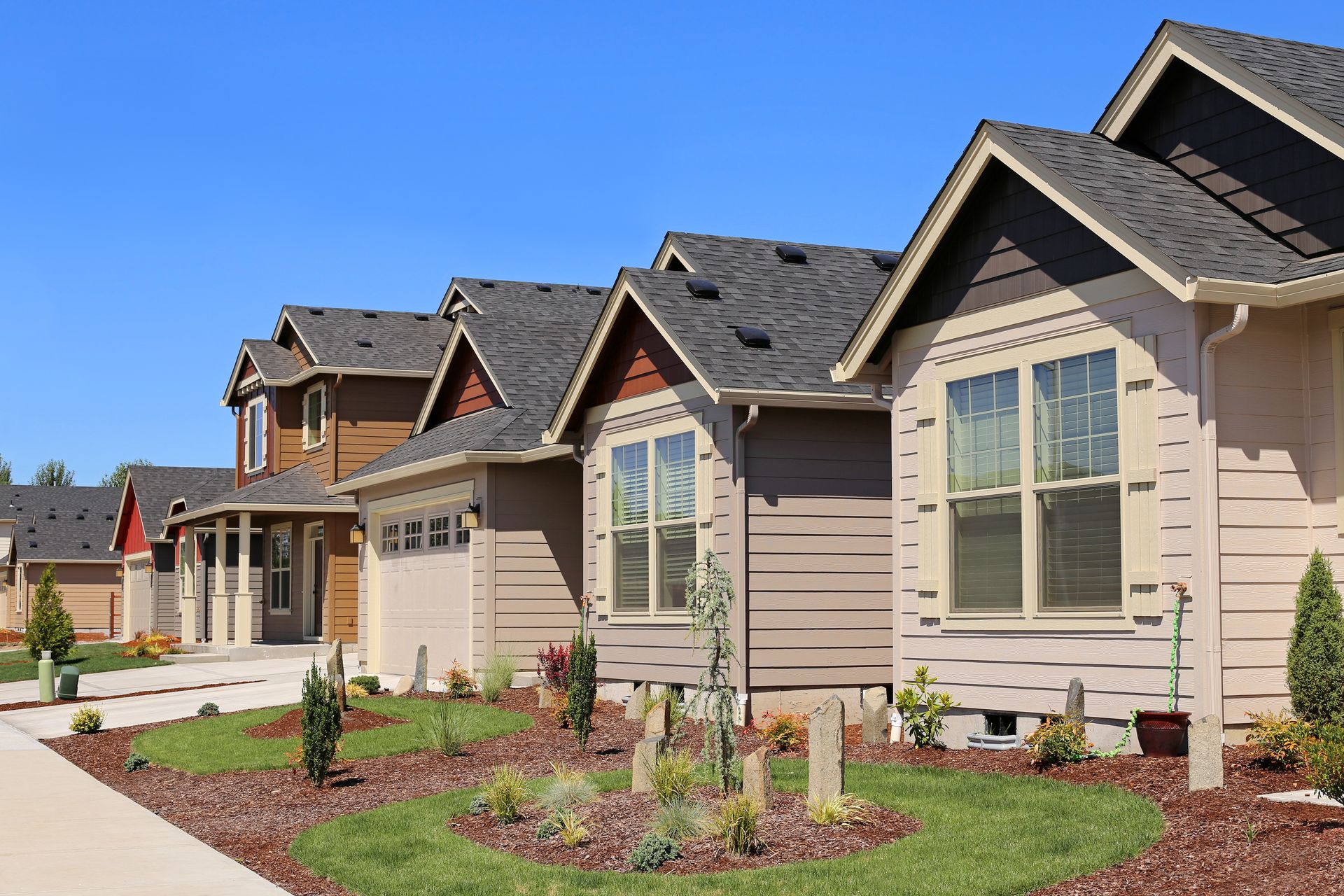 Row of houses with various colored siding, neat landscaping, and clear blue sky.