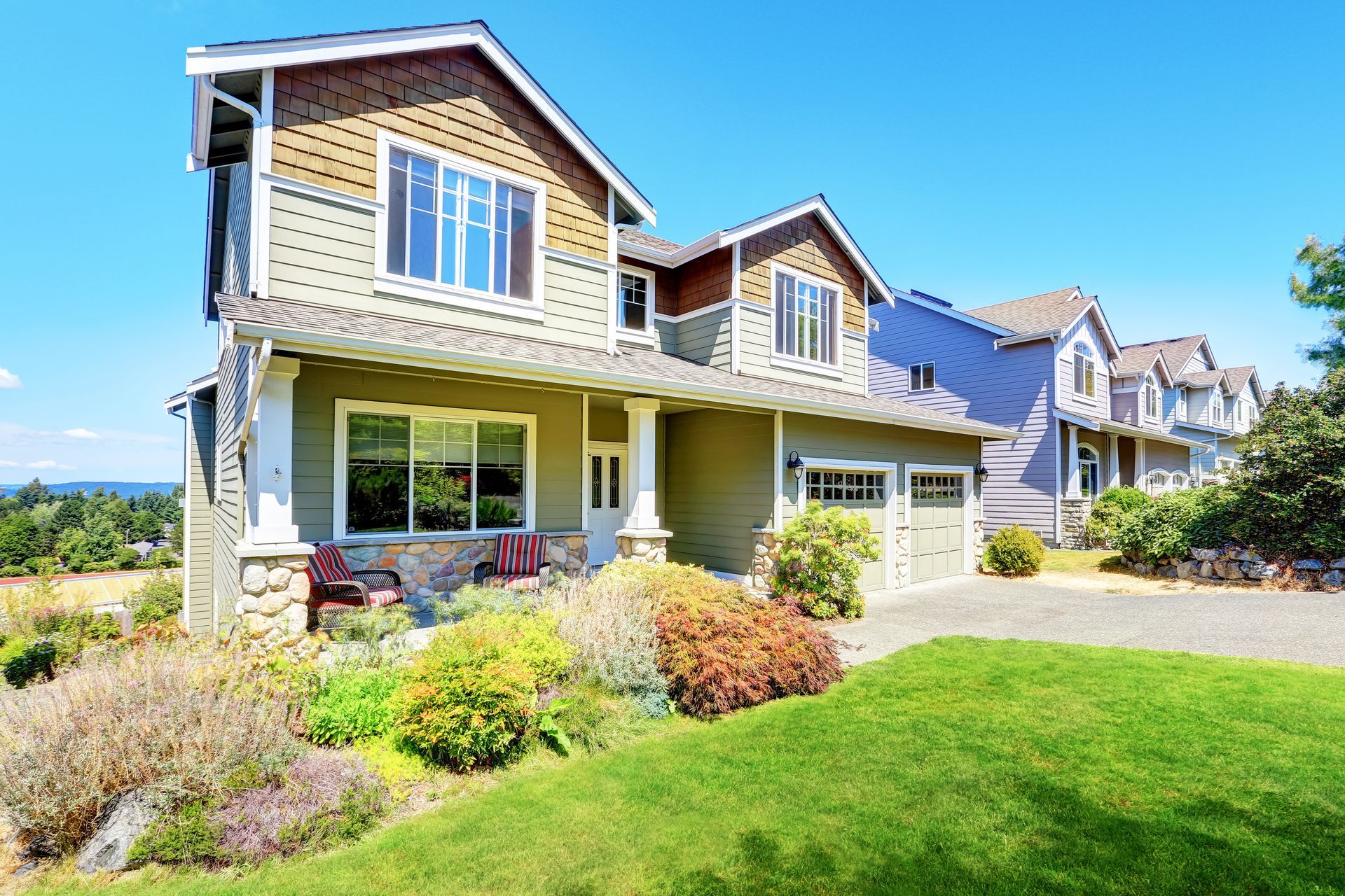 Two-story house with green siding, brown trim, and a small garden, under a bright blue sky.