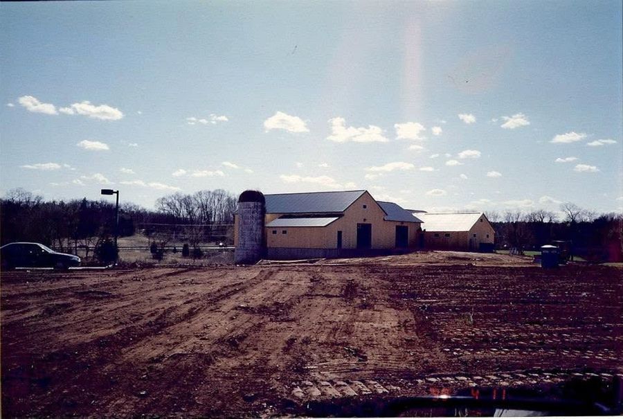 Rural farmstead with white barn and silo under a partly cloudy sky, viewed across a muddy field