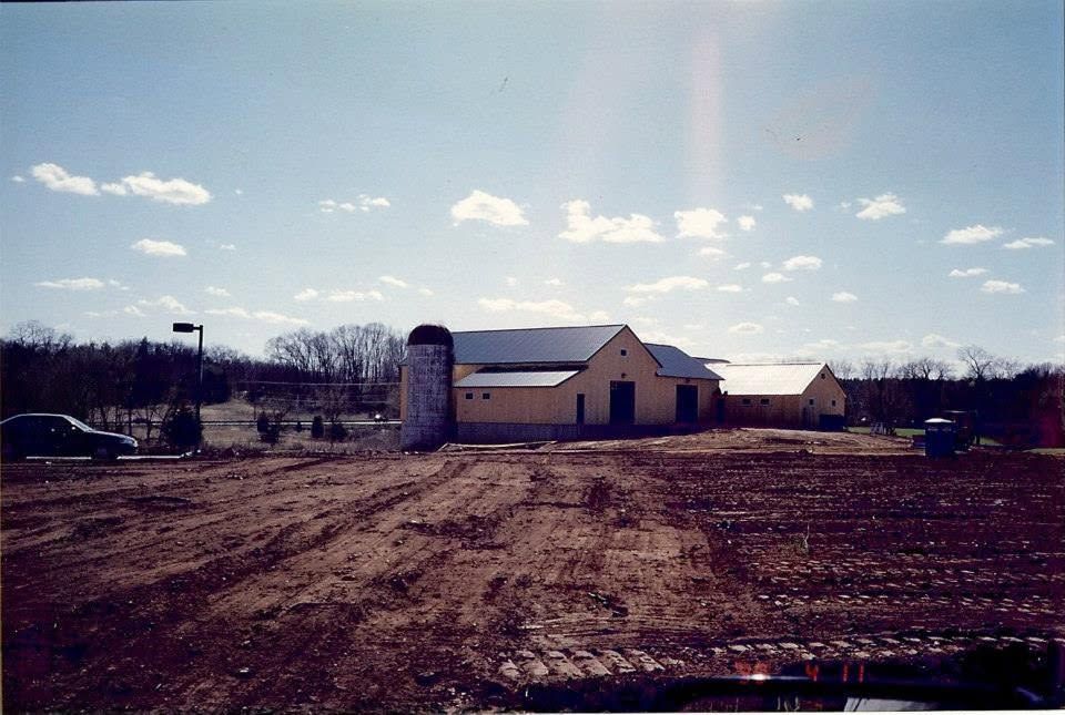 Rural farmstead with a white barn, silo, and dirt field under a partly cloudy sky