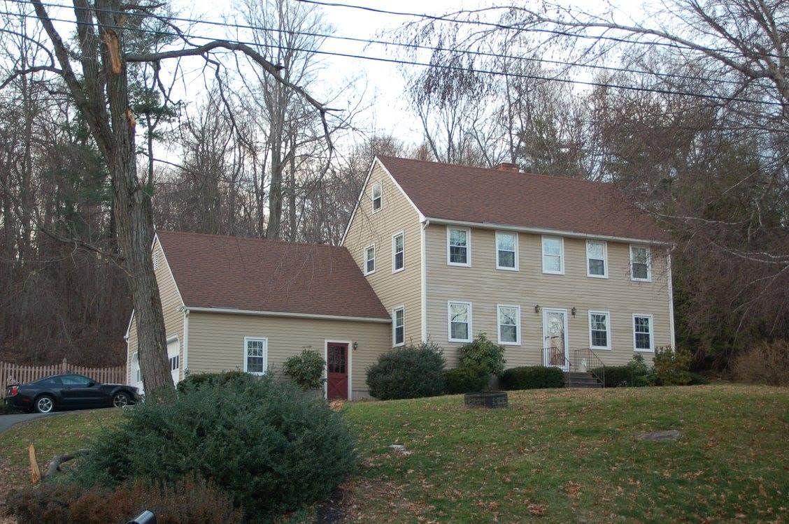 Two beige houses on a wooded hillside, with brown roofs and a grassy yard in front.