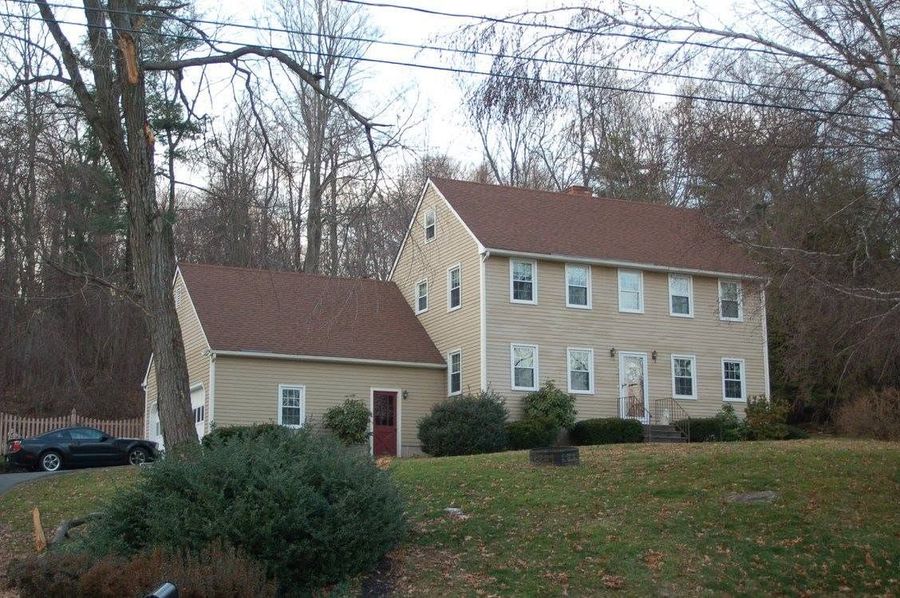 Yellow house with beige garage in a wooded yard, covered in fallen leaves.