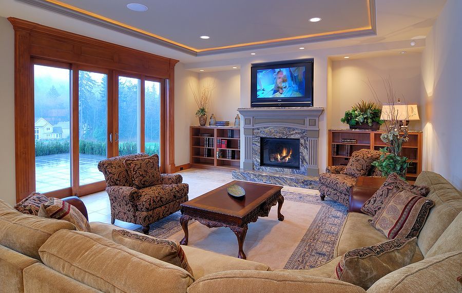 Elegant living room with fireplace, wall-mounted TV, and beige sectional seating by large windows
