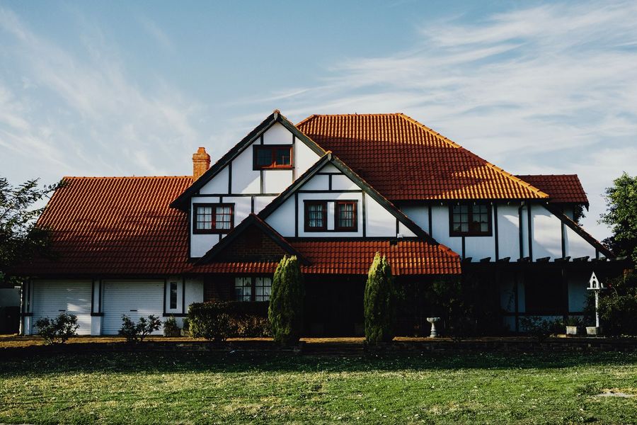 White house with red tiled roof and dark timber trim beside a grassy field under a blue sky