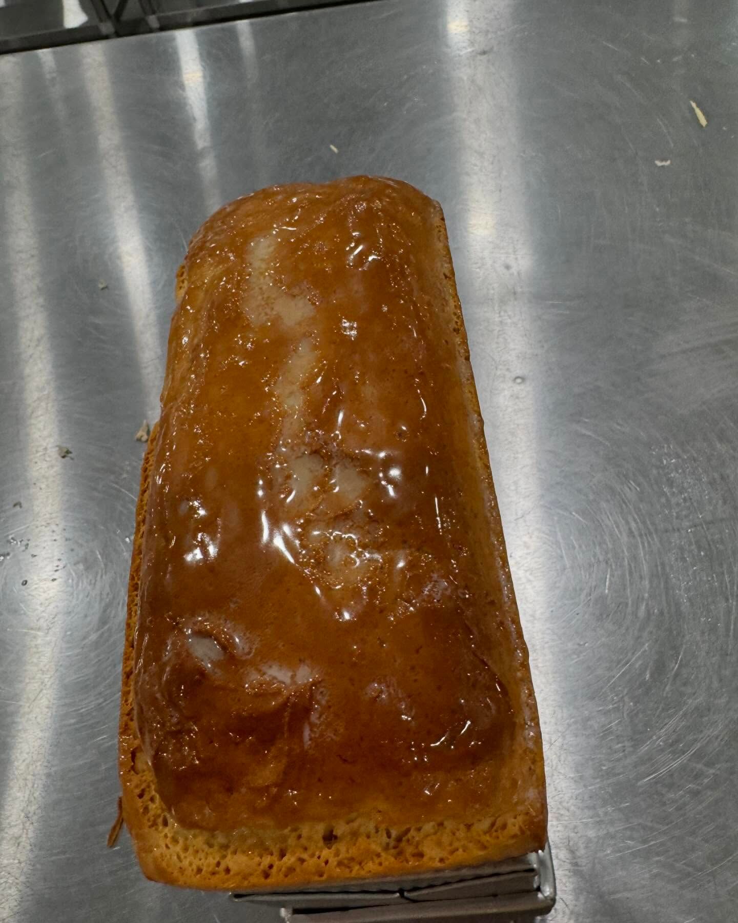 Loaf of golden-brown cake with glazed top, held by a metal spatula.