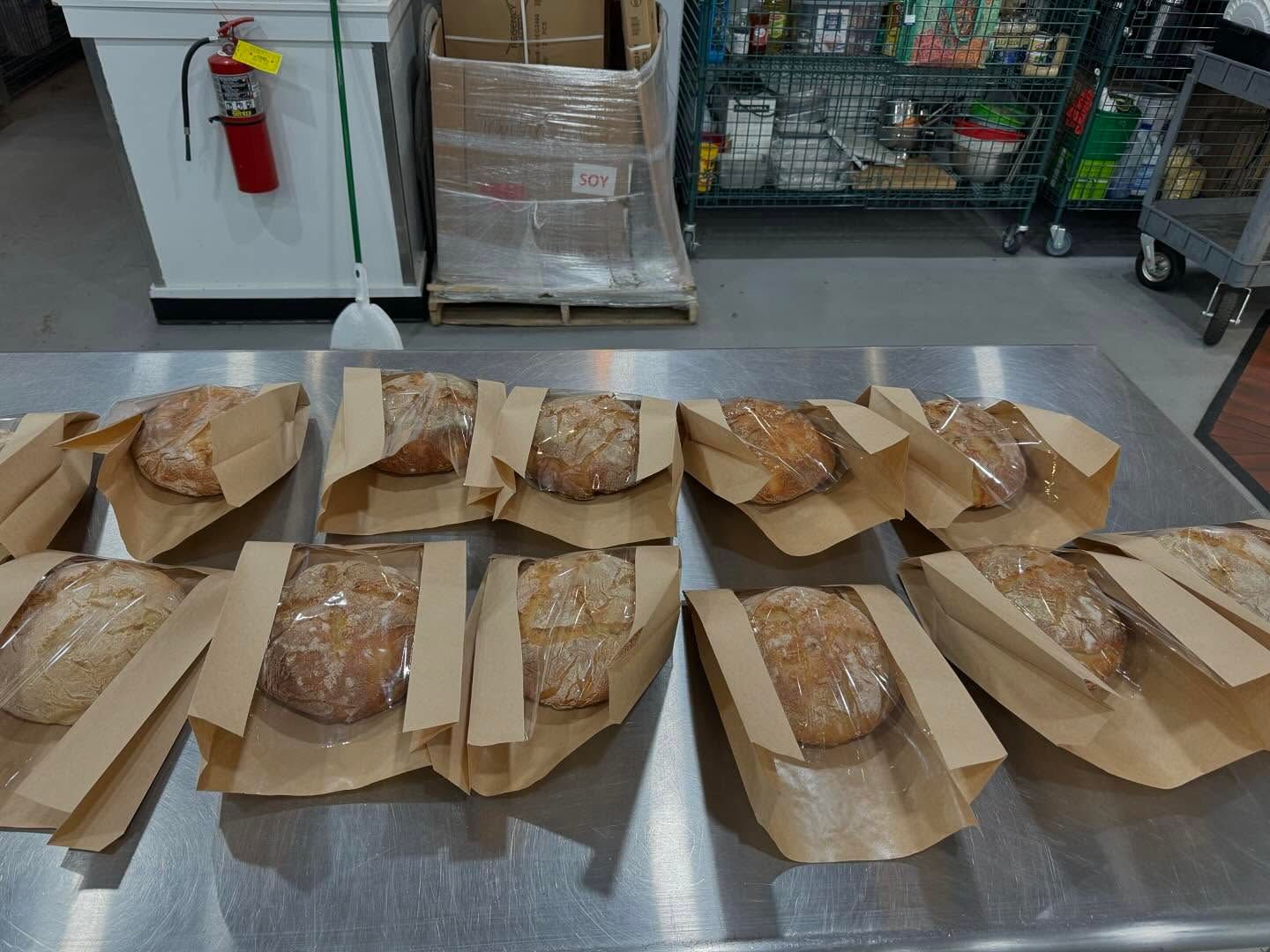 Loaves of bread in paper bags on a stainless steel counter.