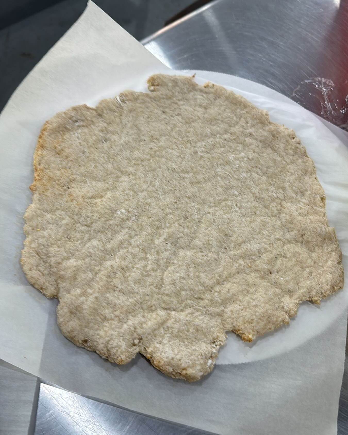 Flat, round, light brown bread on parchment paper, sitting on a metal surface.