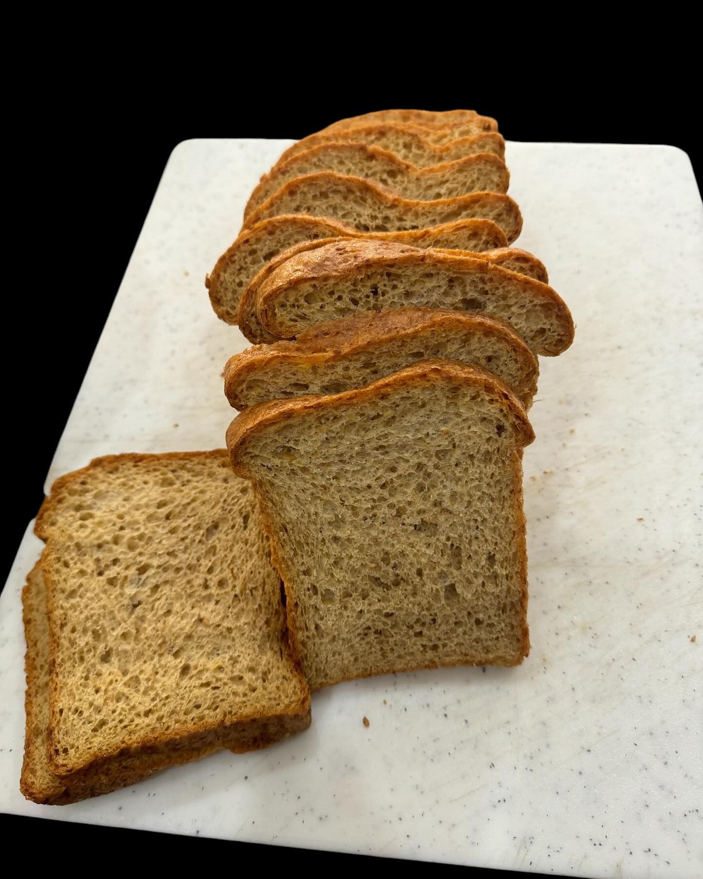 Sliced brown bread on a white cutting board, arranged in a stack.