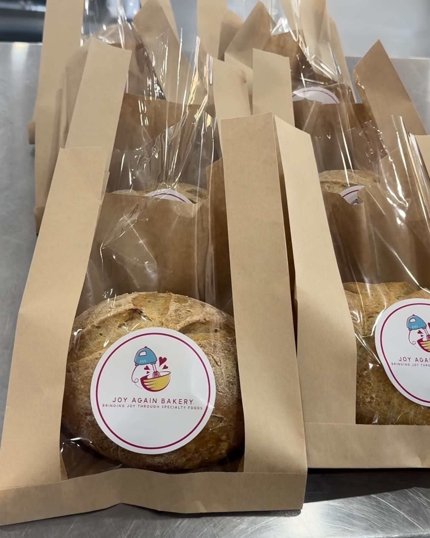 Breads in brown paper bags with clear plastic windows; one with a sticker that says, 