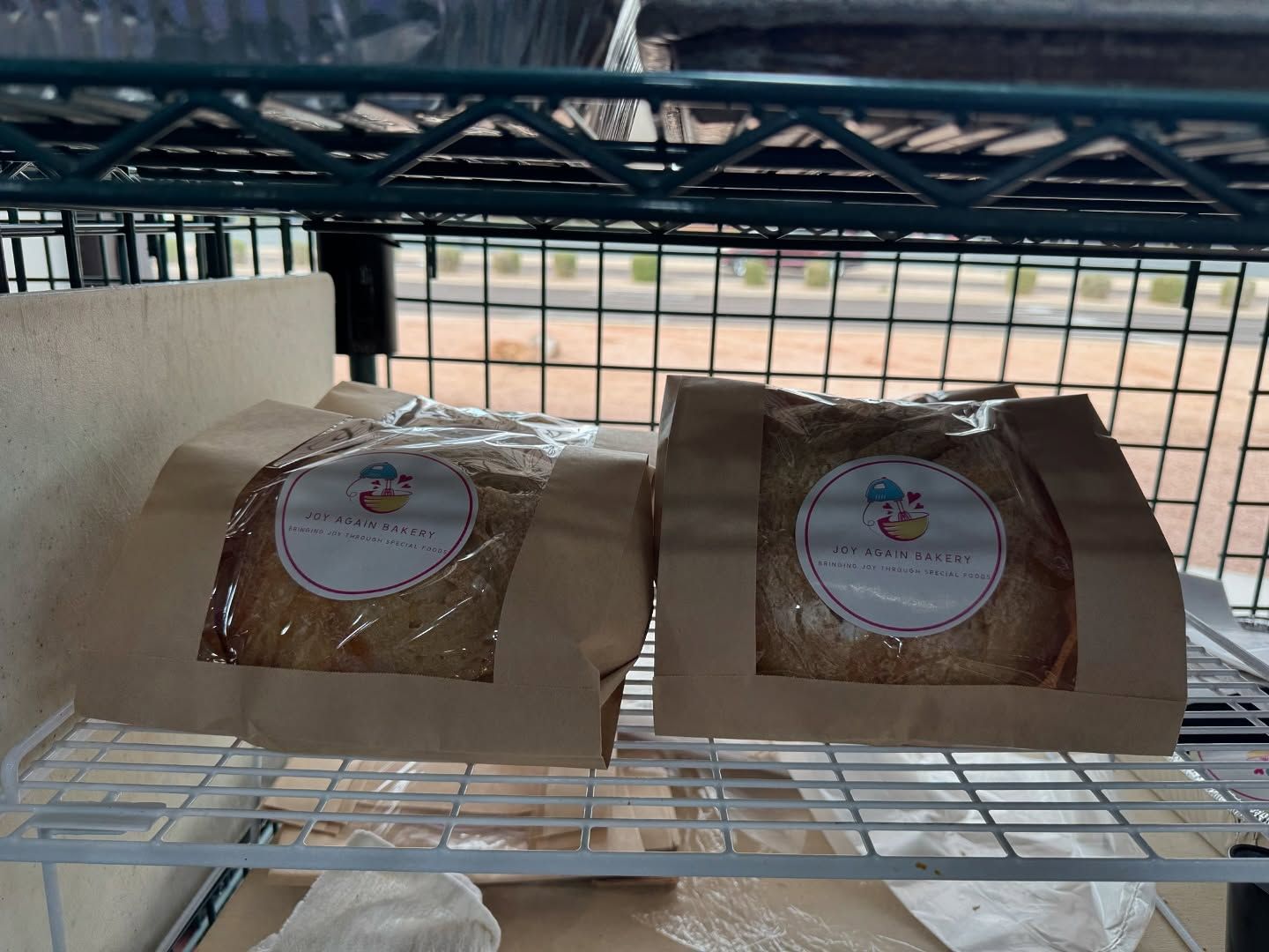 Two loaves of bread in paper bags on a metal shelf, labeled 