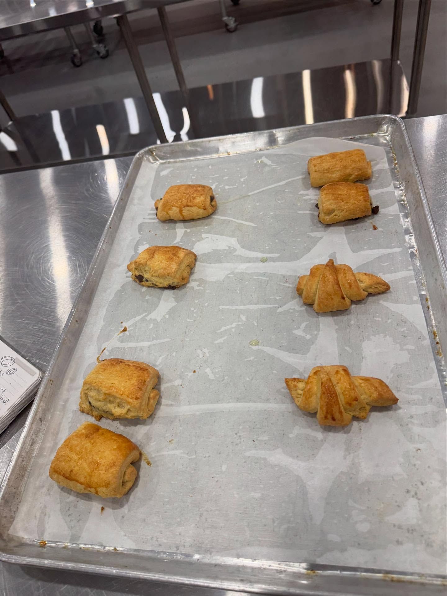 Baked pastries on a baking sheet lined with parchment paper, on a stainless steel surface.