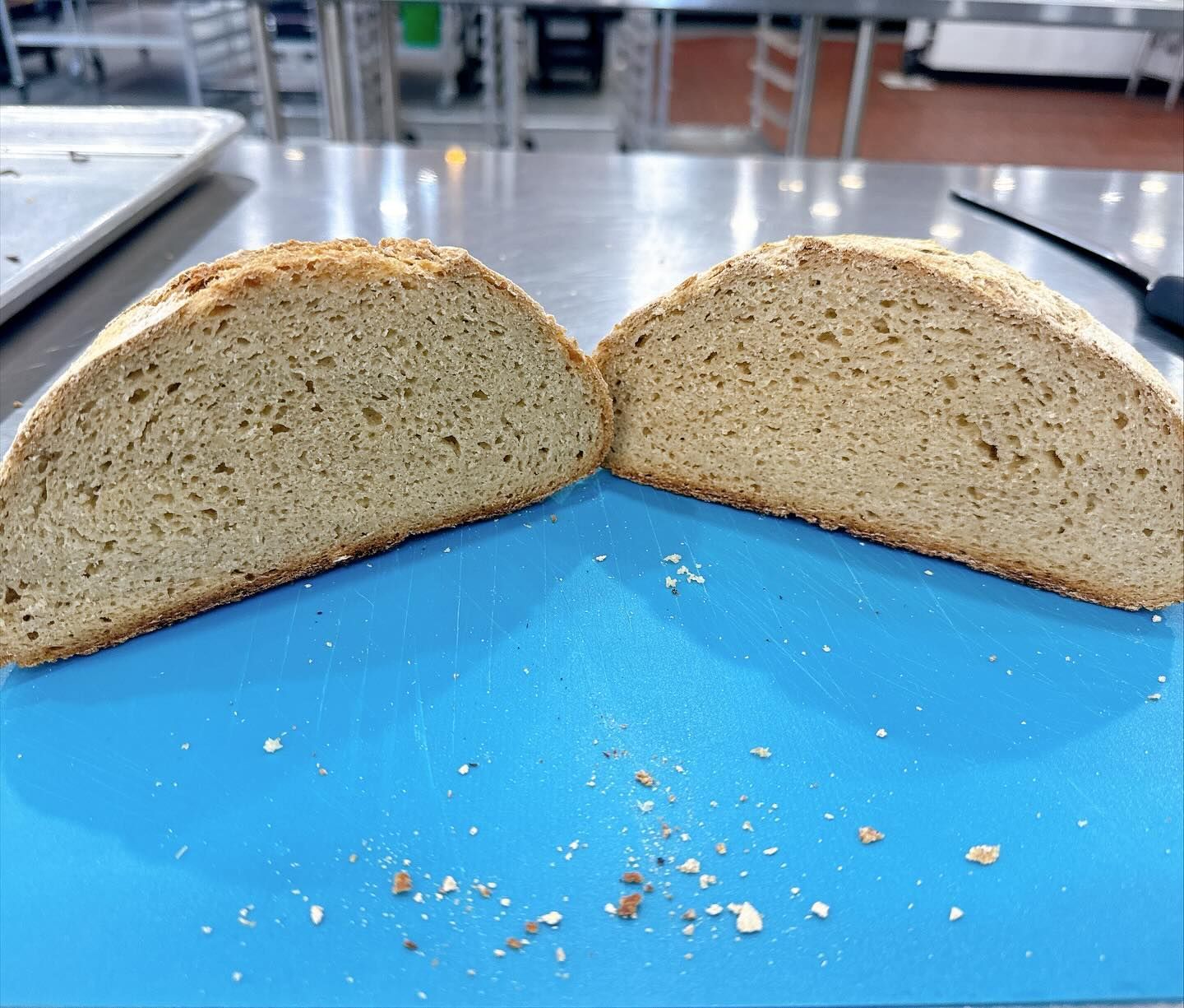 Halved loaf of bread on a blue cutting board, showing interior texture. Crumbs are present.