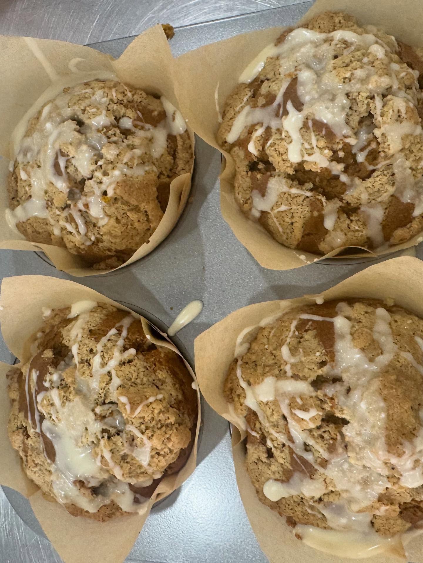 Four muffins in parchment paper cups, topped with crumble and white icing drizzle.