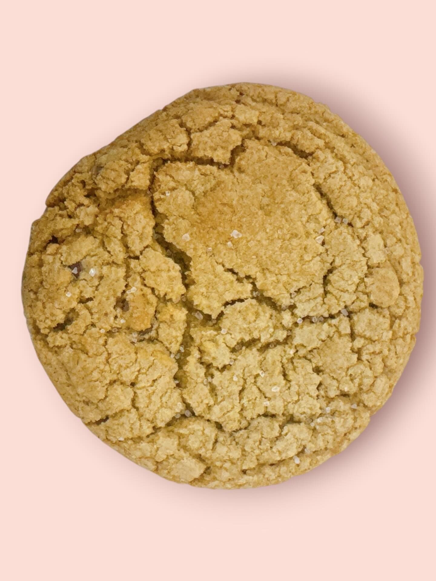 Close-up of a round, textured, golden-brown cookie on a light pink background.