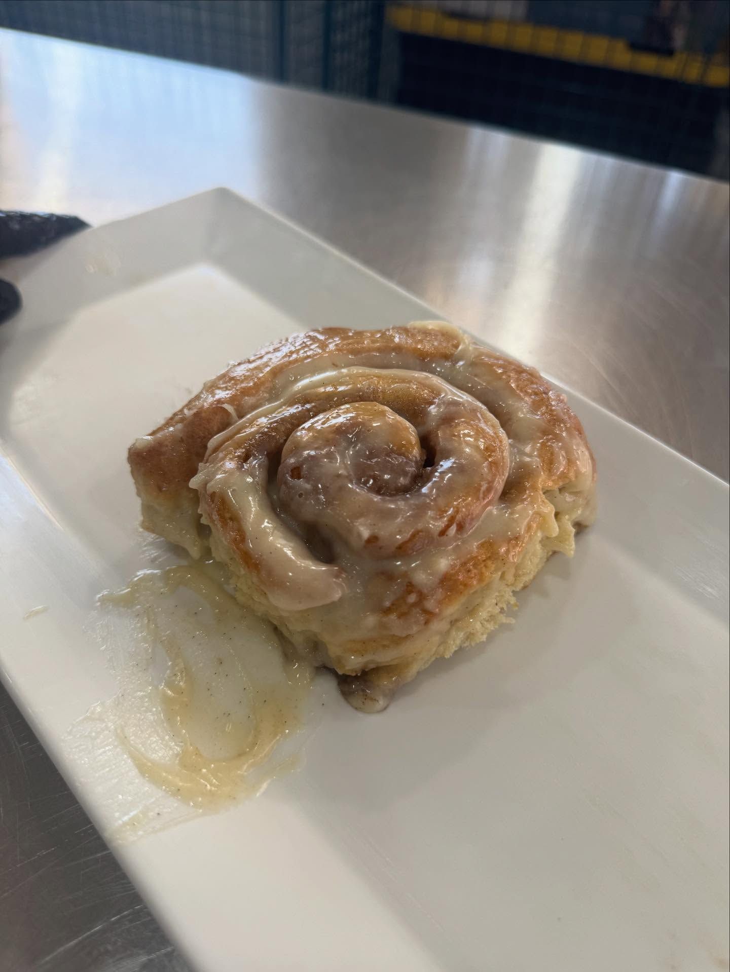 Cinnamon roll with icing on a white rectangular plate, close up.