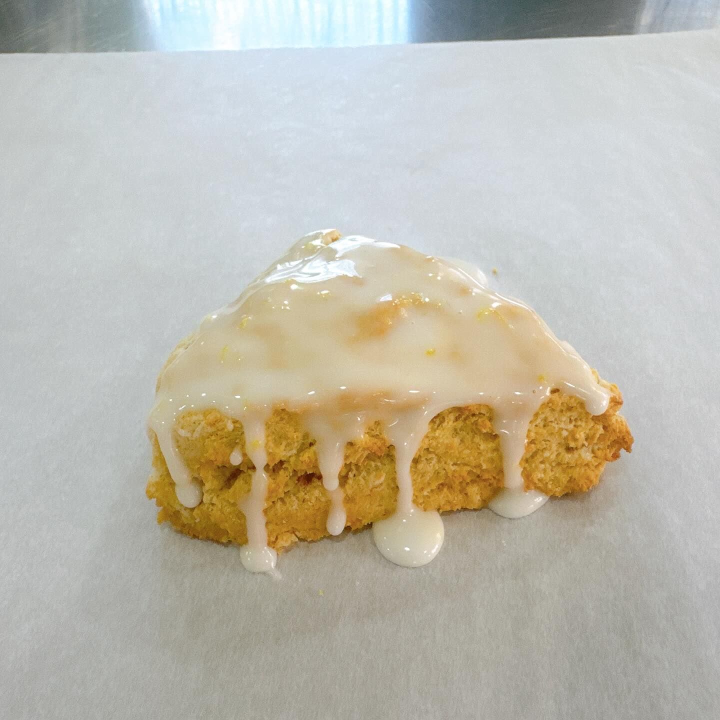 Scone topped with white glaze on white parchment paper.