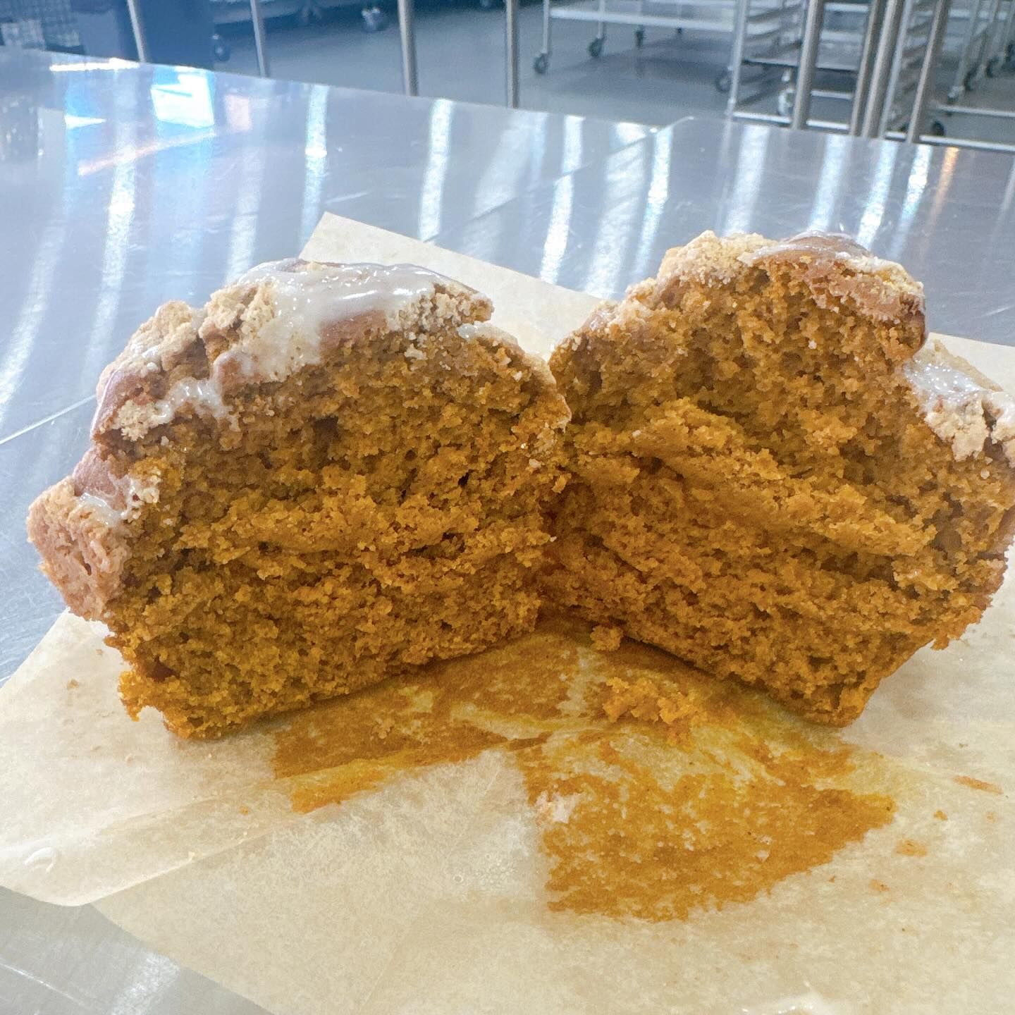 Pumpkin muffin cut in half, on parchment paper, with glazed top.