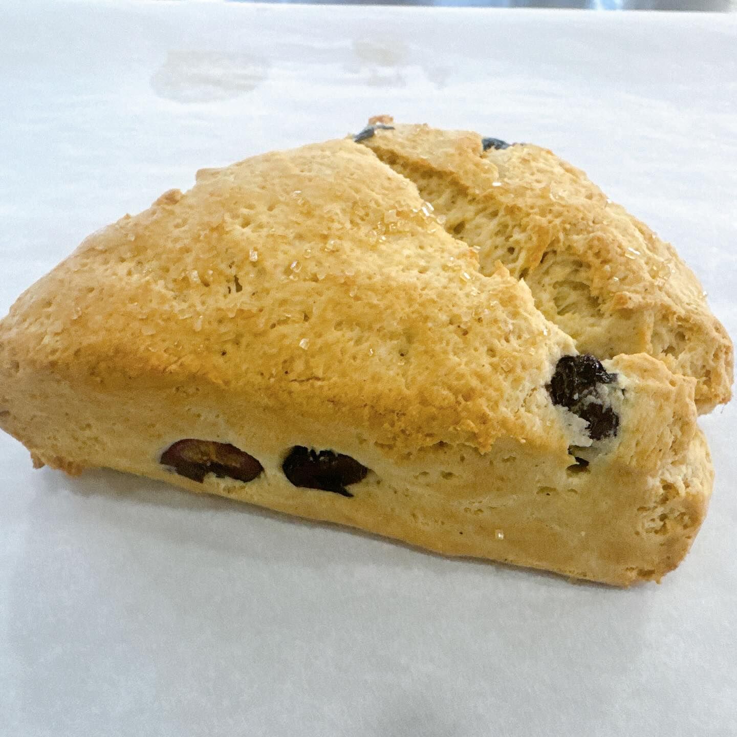 Triangle-shaped scone with raisins on white parchment.