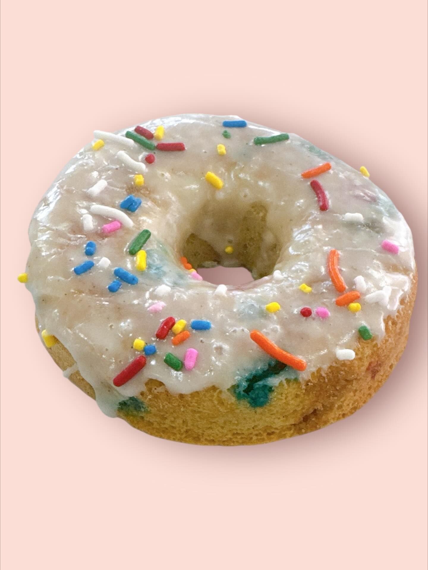 Glazed donut with colorful sprinkles on a pink background.