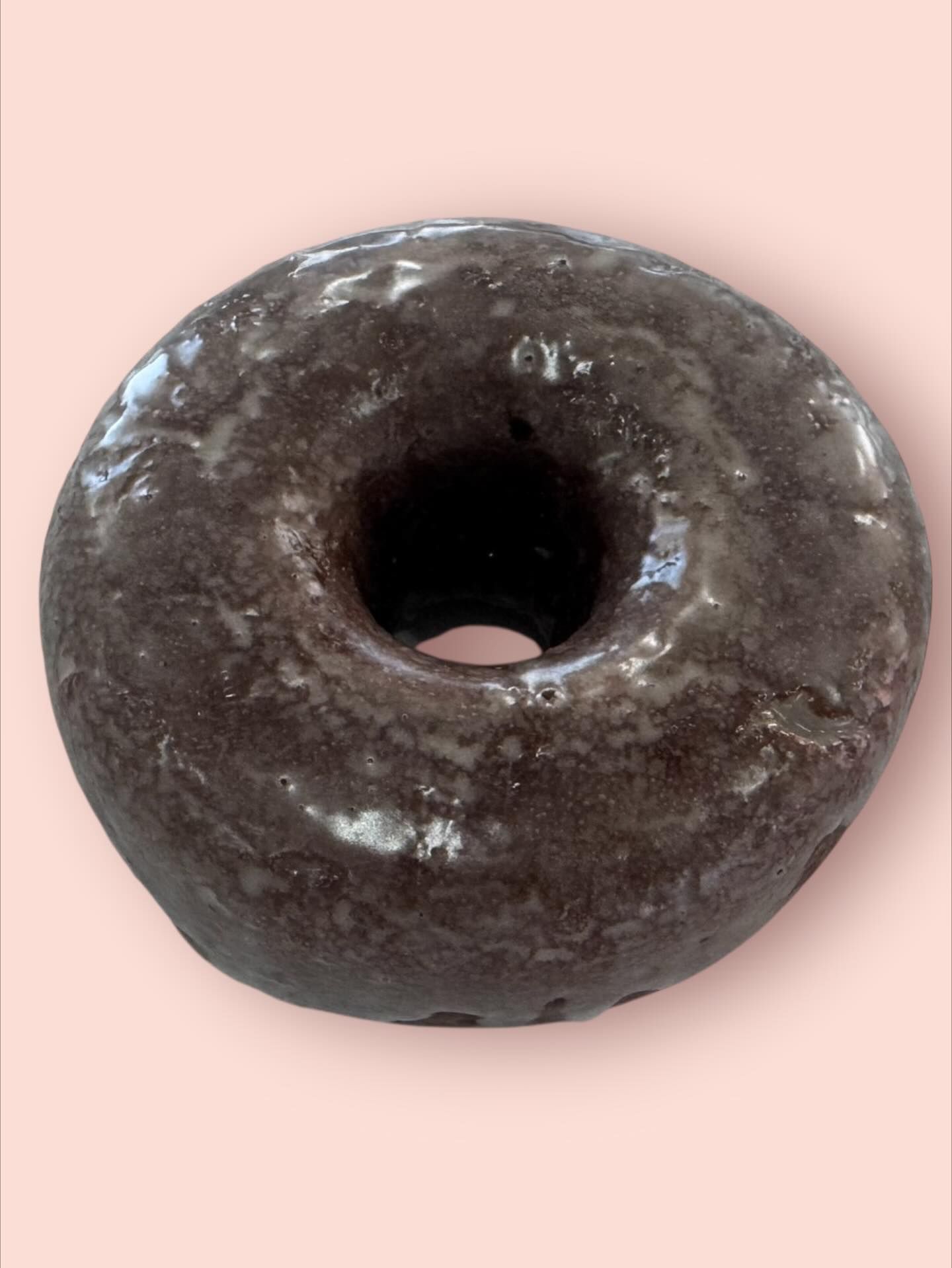 Chocolate glazed donut on a pink background.