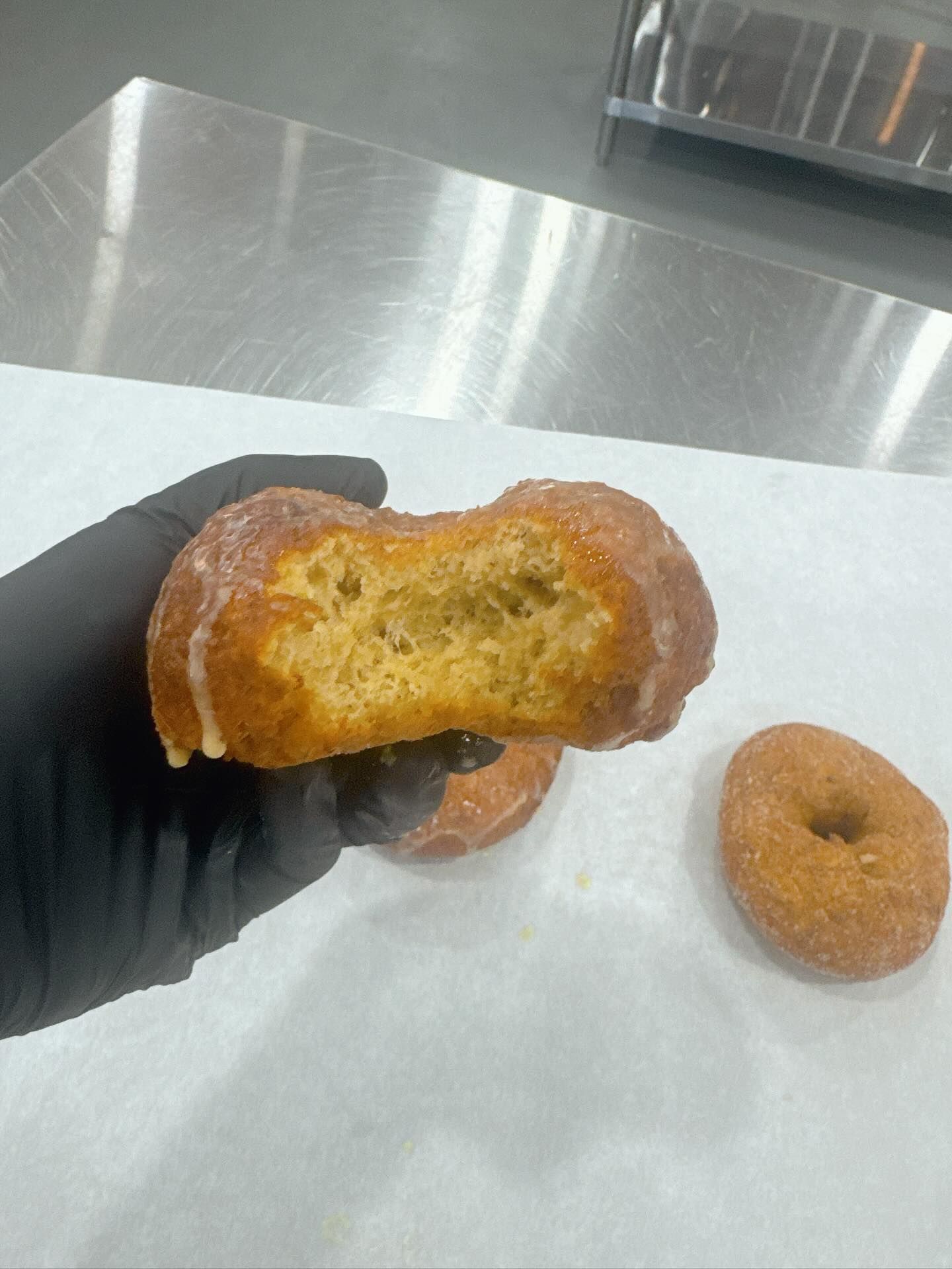 Hand holding a partially eaten donut with glaze, two more donuts on a white surface.