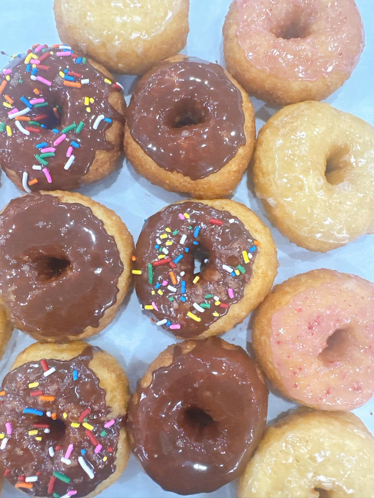 Assortment of glazed donuts, some with chocolate frosting and sprinkles, others with pink or plain glaze.