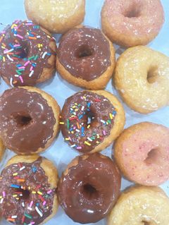 Assortment of glazed donuts, some with chocolate frosting and sprinkles, others with pink or plain glaze.