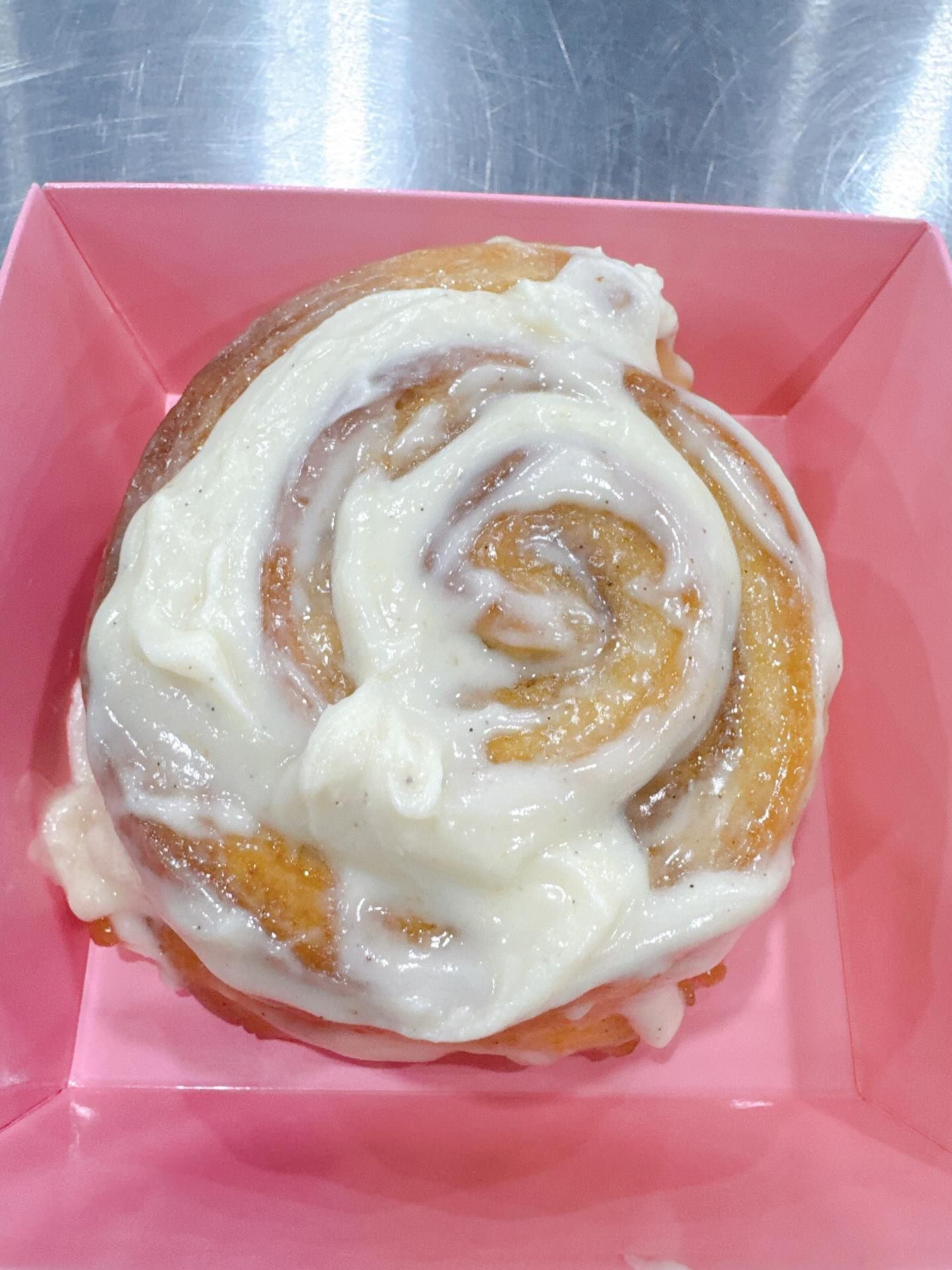 Cinnamon roll with white icing in a pink container.