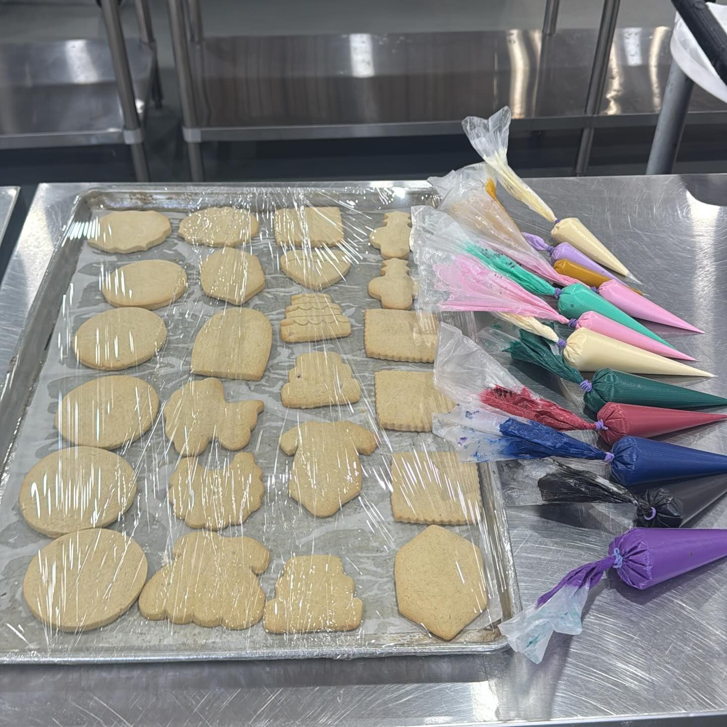 Cookies on a tray with colorful piping bags on a metal surface.