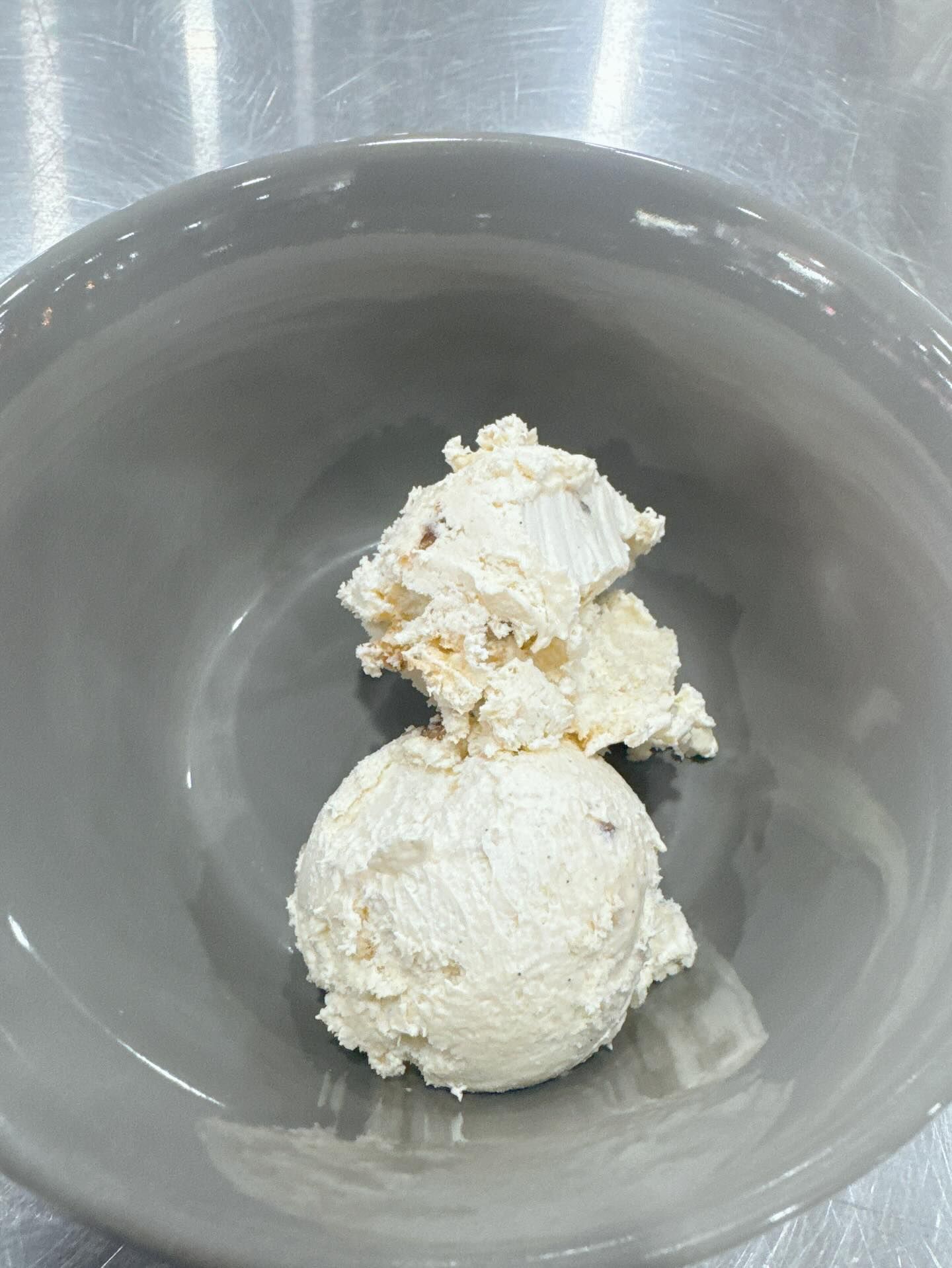 Light-colored scoop and pile of creamy food in a gray bowl on a silver surface.